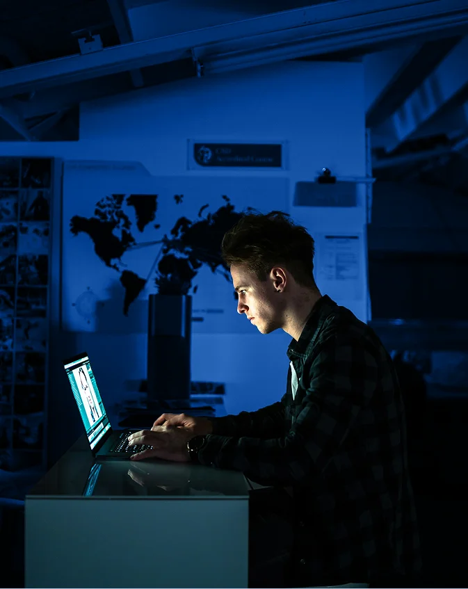 Analyste en cybersécurité surveillant des données sur son ordinateur la nuit devant une carte du monde