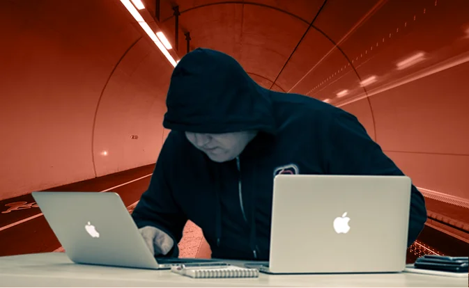 Homme encapuchonné manipulant deux ordinateurs portables dans un tunnel, illustrant l'usurpation d'identité en ligne